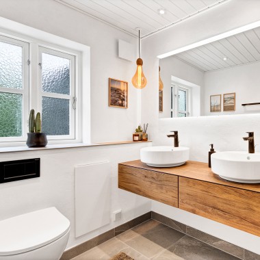 İki yuvarlak lavabo, büyük bir ayna ve ahşap banyo mobilyaları içeren aydınlık, yenilenmiş banyo (© @triner2 and @strandparken3)