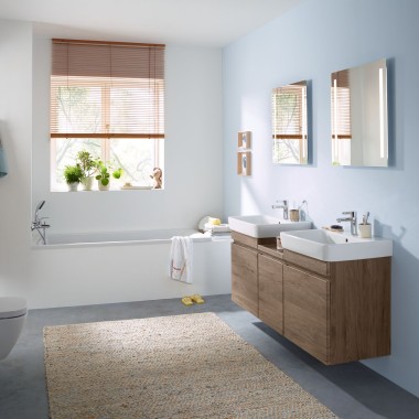Açık mavi duvar ve Geberit aynalı dolap, kumanda kapağı, vitrifiye ve ceviz renginde banyo mobilyaları